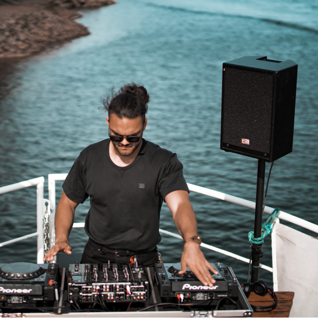 DJ performing on a deck during Canada Day Cruise Ottawa with equipment and speaker in scenic waterfront setting.