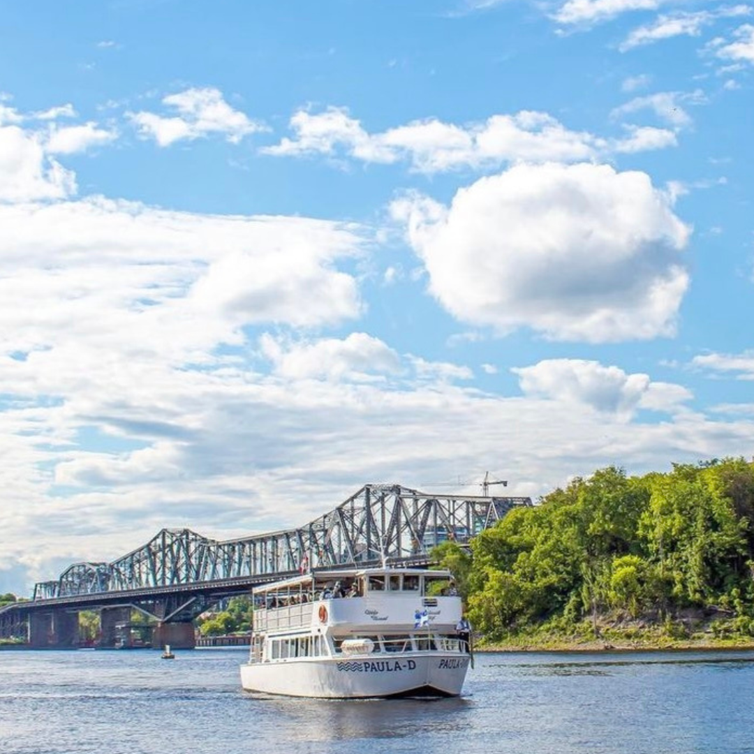 2-Day Hop-On Hop-Off & River Cruise boat cruising on a river with a bridge and blue sky in the background.